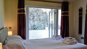 Una habitació d'hotel amb un llit, una tauleta de nit, una làmpada, una finestra amb cortines i vista a un paisatge rocosós.