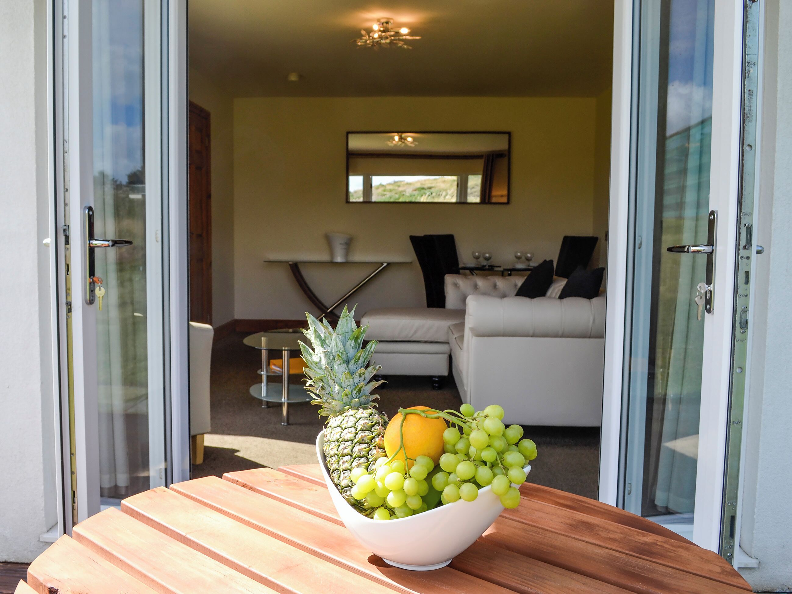 A dining area with a table holding a bowl of fruit, a sofa, and a dining table in the background.