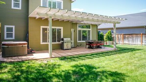 Un jardin avec un patio couvert, un jacuzzi et un barbecue.