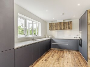 Una cocina moderna con armarios oscuros, una encimera de madera y un ventanal con vistas a zonas verdes.