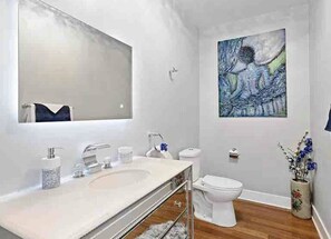 Um banheiro moderno com um espelho grande, acessórios brancos, piso de madeira e um quadro na parede.