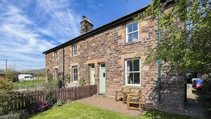 A stone house with a front porch, a wooden fence, and a grassy yard.