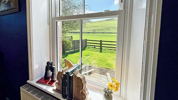 A window with a view of a green field and a wooden fence.