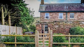 A stone house with a wooden gate, a gravel driveway, and a 'Welcome' sign.