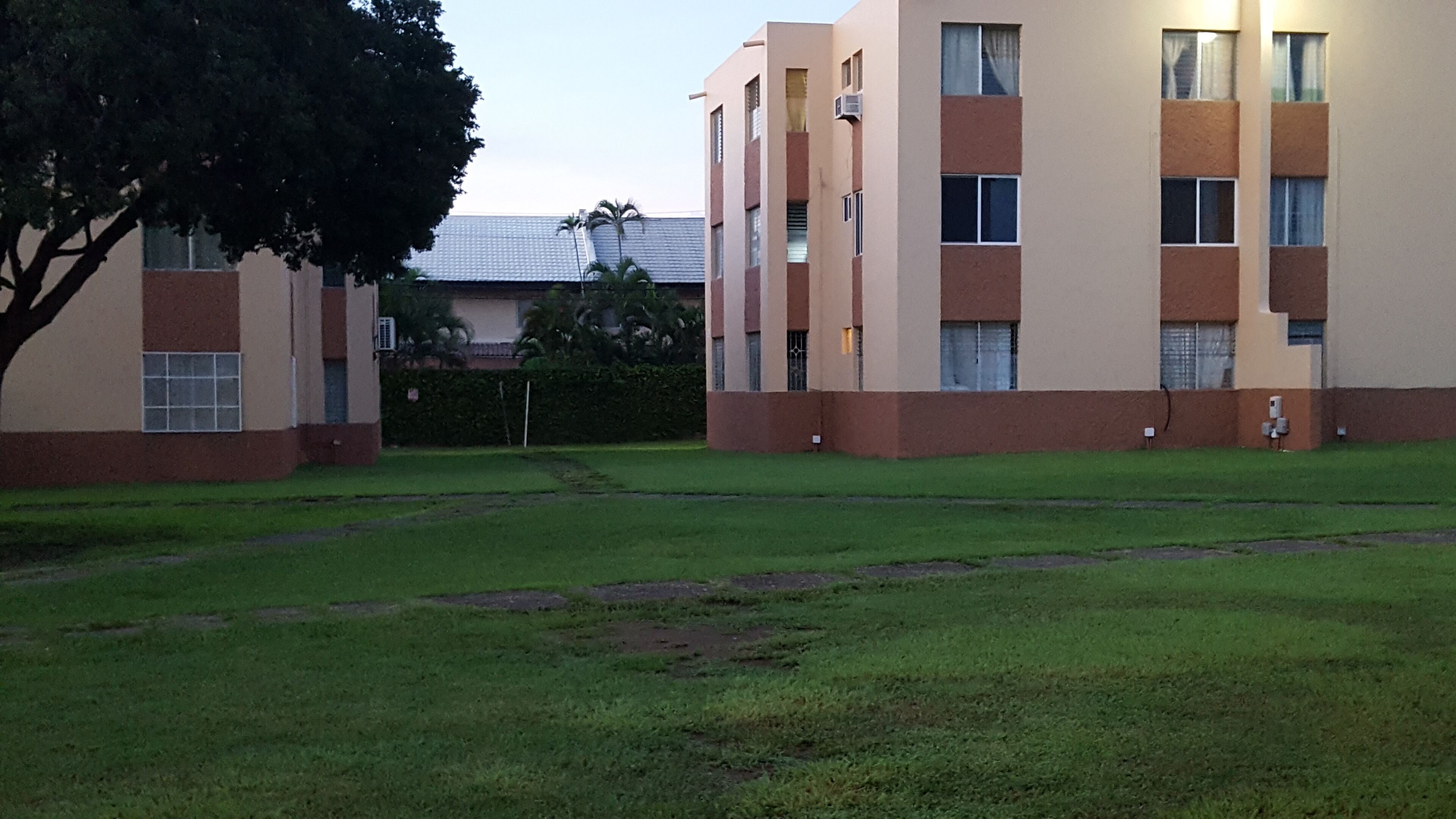 A building with multiple windows and a flat roof, surrounded by a grassy area.