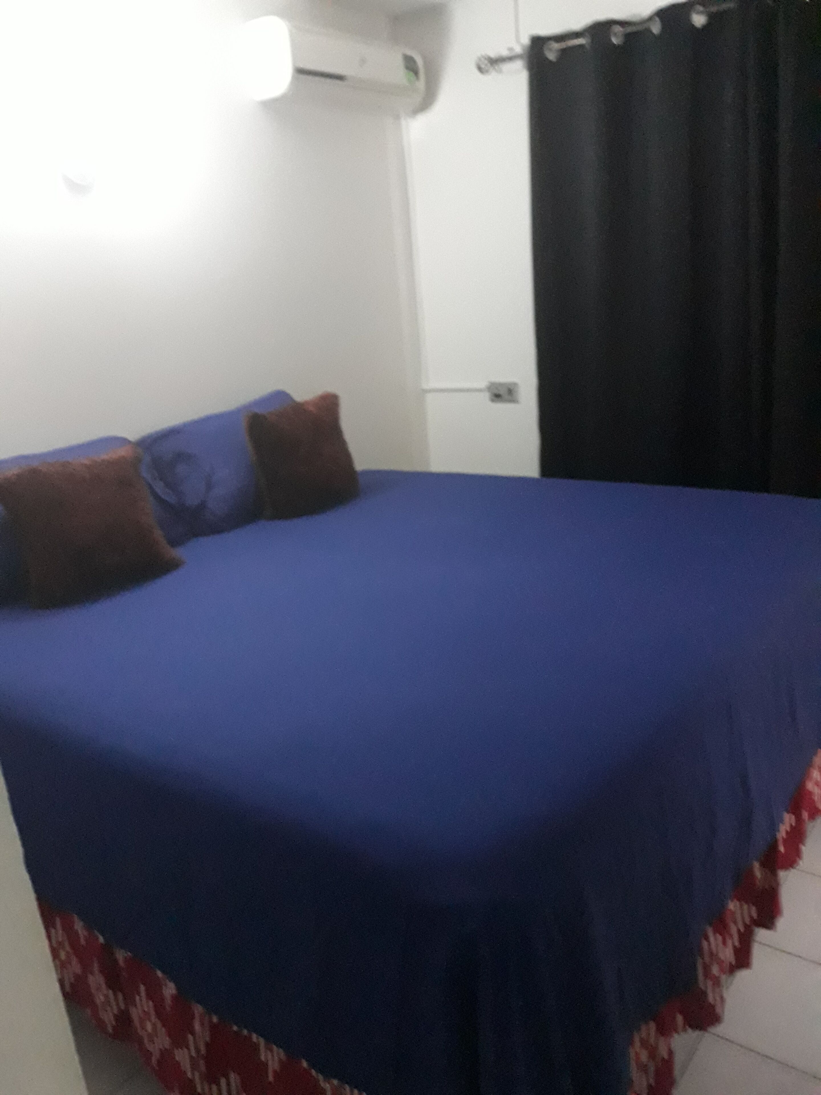 Une pièce comprenant un lit, un climatiseur fixé au mur, un rideau et un luminaire.
