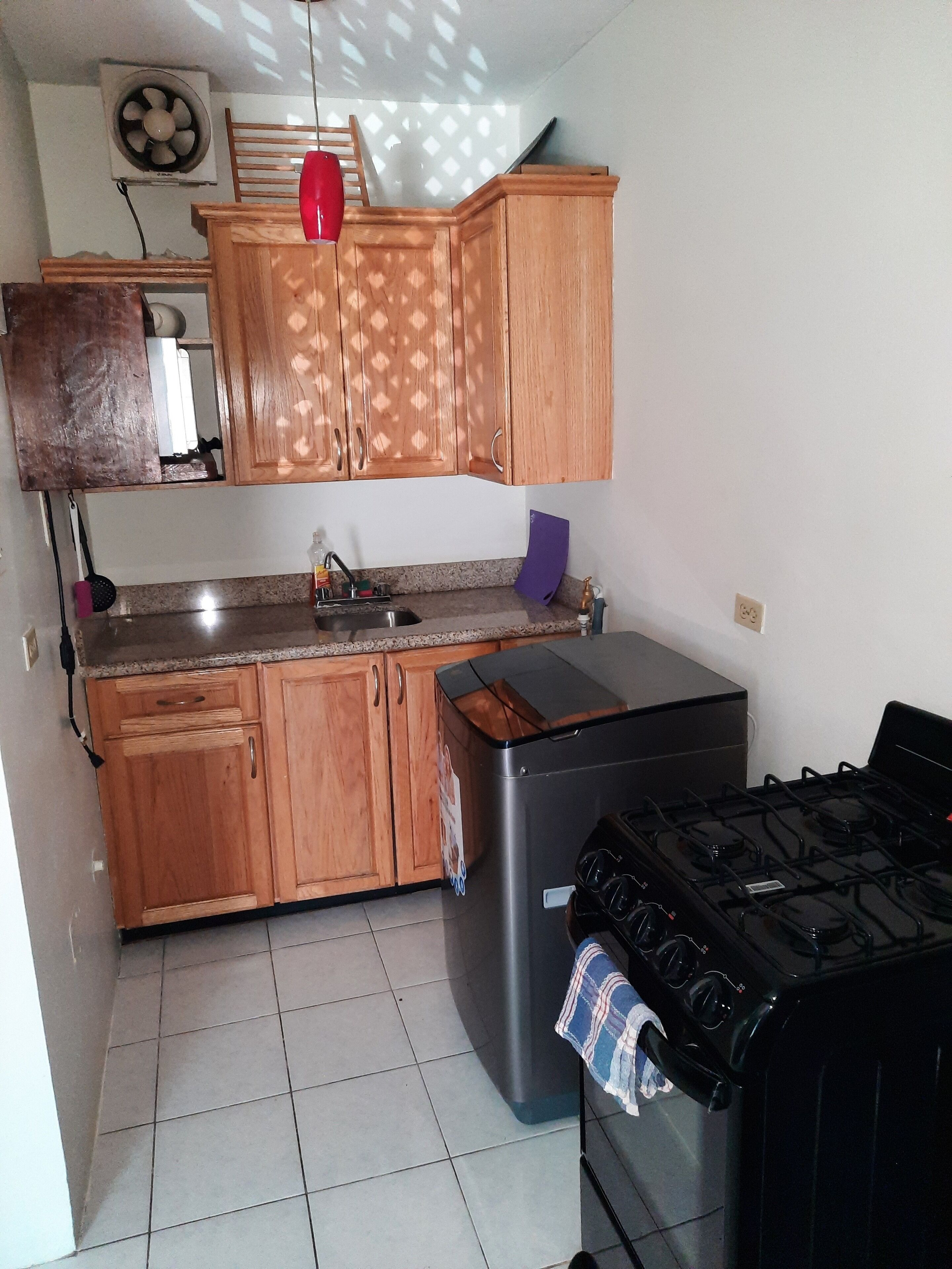 Una cocina con armarios de madera, un lavamanos de acero inoxidable, un refrigerador y una estufa a gas.