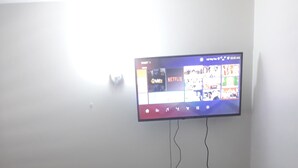 A living room with a mounted TV displaying a streaming service interface, a laptop on a stand, and a couch. - Cozy vacation apartment in Kingston (Kingston)
