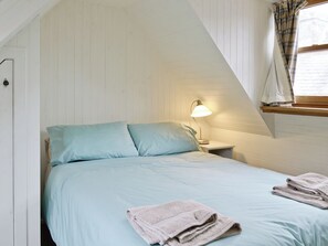 Quarto com cama, almofadas, mesa de cabeceira, abajur e janela com cortinas.