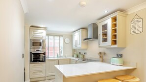 Een moderne keuken met witte kastjes, een centraal keukenblok met krukken, een ingebouwde oven en een klok aan de muur.