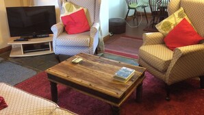 Ein Wohnzimmer mit Fernseher, zwei gemusterten Sesseln, einem Couchtisch und einem roten Teppich.
