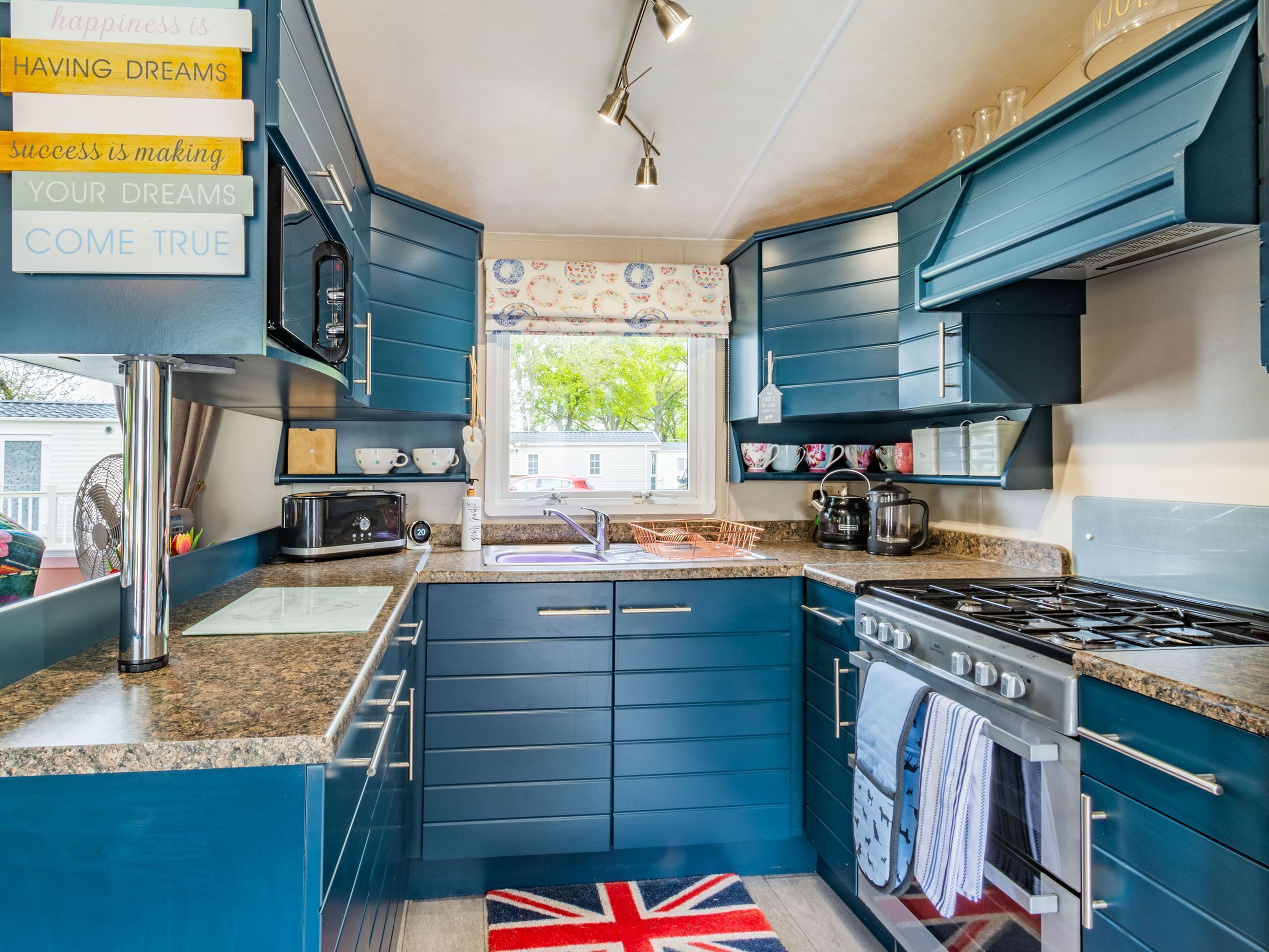 A modern kitchen with blue cabinets, a gas stove, a microwave, and a sink.