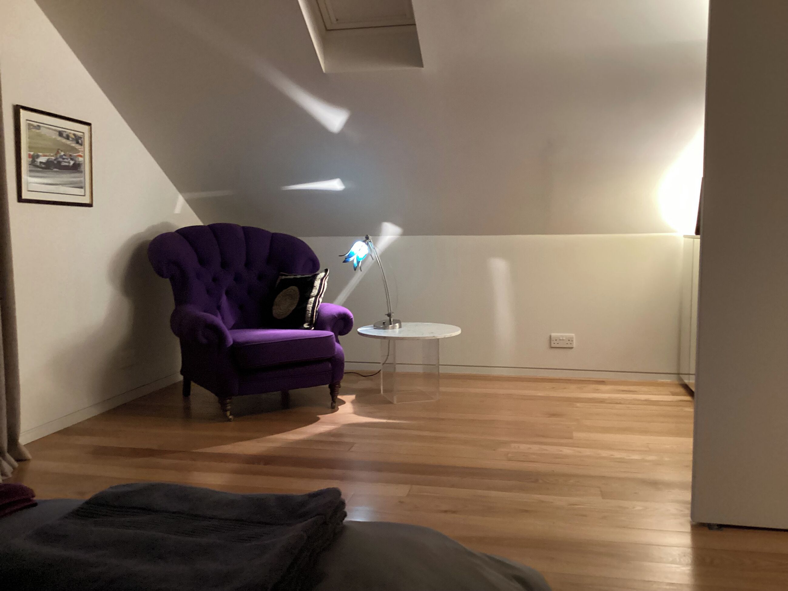 Um quarto com uma poltrona roxa, uma mesa redonda pequena e uma luminária.