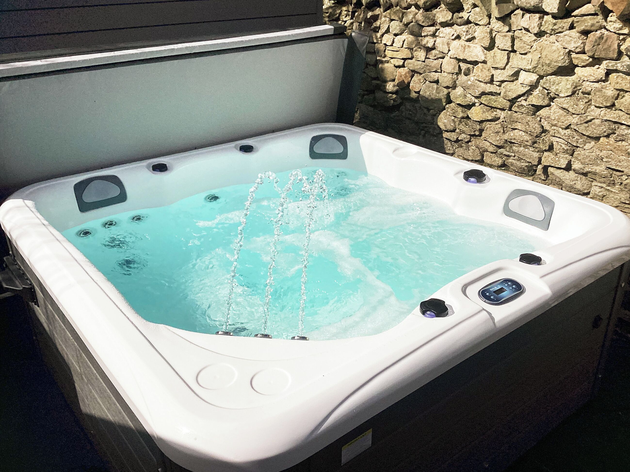 A hot tub with a stone wall backdrop, control panel, and jets.