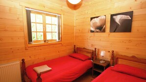Une chambre dans un chalet en bois, avec deux lits, une fenêtre et un radiateur.