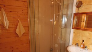 Un intérieur en bois avec une douche en verre, un meuble en bois doté d’un miroir et un lavabo avec des articles de toilette.
