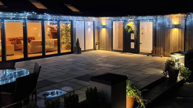 A patio area with a seating arrangement, a small Christmas tree, and a door with a hanging plant. - 1 bedroom accommodation in North Rode (North Rode)