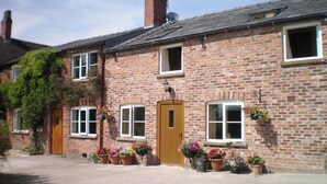 A brick building with a wooden door, multiple windows, and potted plants. - 1 bedroom accommodation in North Rode (North Rode)