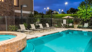 A swimming pool with lounge chairs and a hot tub area, surrounded by a fence and outdoor lighting.