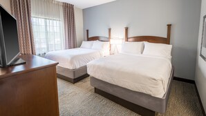 A hotel room with two beds, a desk with a laptop, and a large window with curtains.