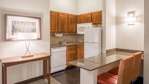 A compact kitchen with wooden cabinets, a white refrigerator, a microwave, and a granite countertop.