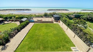 A backyard with a lawn, a pool, and a view of the beach.