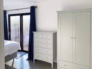Une chambre à coucher comprenant un lit, une commode blanche, une armoire et une porte-fenêtre coulissante donnant sur un espace extérieur.