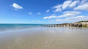 A beach with a wooden pier extending into the water, clear skies, and calm sea.