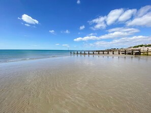 Une plage avec une jetée en bois qui s’avance dans l’eau, un ciel dégagé et une mer calme.