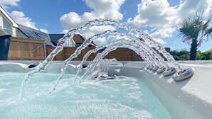 A hot tub with water jets, a wooden deck, and a clear sky.