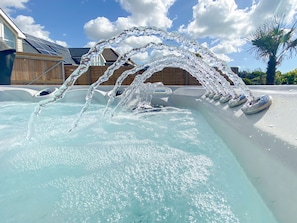 Un bain à remous avec jets d’eau, une terrasse en bois et un ciel dégagé.