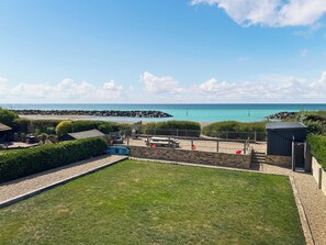 Une cour verdoyante avec une piscine, un petit abri de jardin et une vue sur la mer.