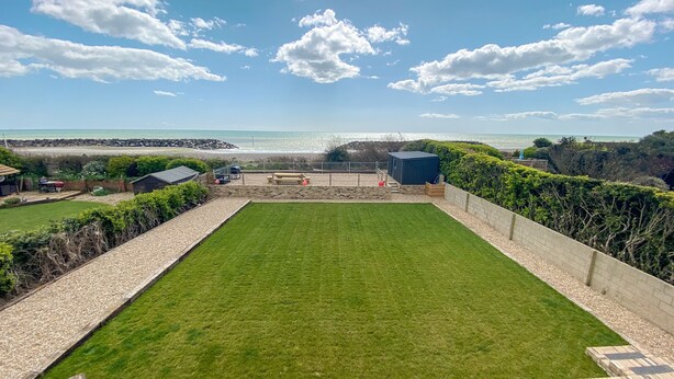 A well-maintained lawn with a patio area, a small shed, and a view of the sea.