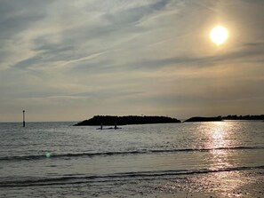 Une mer calme, le soleil se reflétant sur l’eau, une île lointaine et un phare.