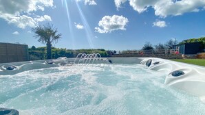 A hot tub with multiple jets, surrounded by a fenced yard with a palm tree and a building in the background.