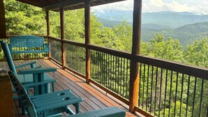 A wooden deck with picnic tables and a bench overlooking a forested mountain landscape.