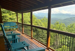 A wooden deck with picnic tables and a bench overlooking a forested mountain landscape.