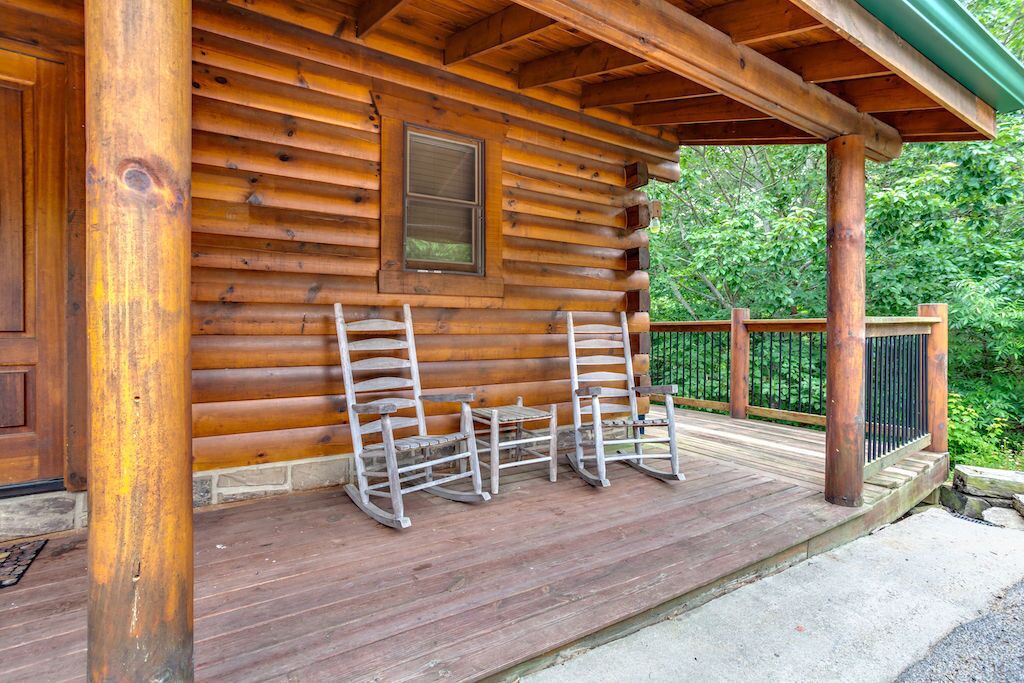 A log cabin with a porch, two rocking chairs, and a wooden deck.