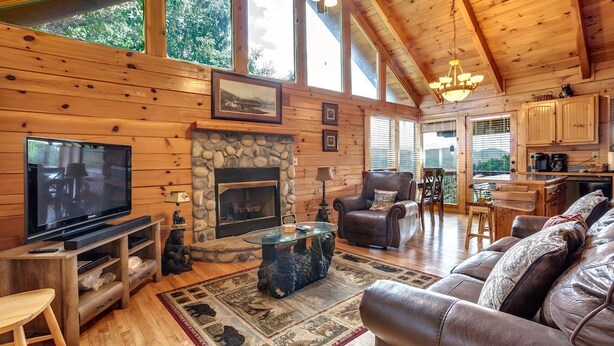A cozy cabin interior with a stone fireplace, leather furniture, and a television.