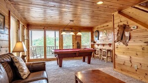 A cozy room with a pool table, leather sofa, and a wooden ceiling.