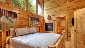 A wooden cabin bedroom with a bed, a fireplace, and a television.