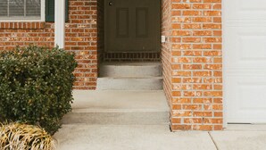 Une maison en briques avec une porte d’entrée, une fenêtre avec des volets, un petit porche et une lanterne fixée au mur.