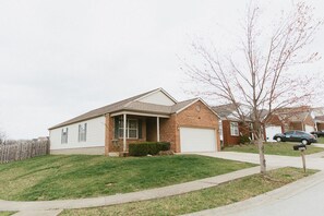 A single-story brick house with a front porch, a garage, and a well-maintained lawn.