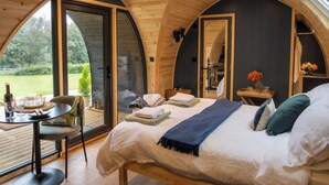 A cozy bedroom with a large bed, a small table, and a chair. There is a window with a view of the outdoors. - Peace and quiet, sat in the middle of your own field with a private hot tub. (Leadburn, near West Linton)