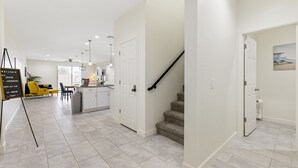 Une cuisine moderne avec des meubles blancs, une chaise jaune et un escalier.