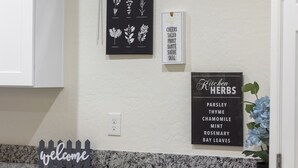 Un mur de cuisine orné d’une pancarte d’accueil, d’un tableau noir illustré de motifs végétaux et d’une autre pancarte indiquant les herbes aromatiques utilisées en cuisine.