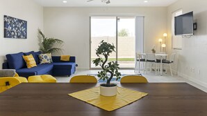 Un salon moderne comprenant un coin repas, un ventilateur de plafond, une plante en pot et un téléviseur fixé au mur.