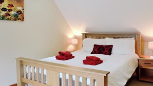 A bedroom with a wooden headboard, a white bedspread, two red towels, a red pillow, and a painting on the wall. - A beautiful barn conversion set within the grounds of a working farm. (Benmore near Dunoon)