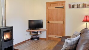 A living room with a fireplace, a television on a shelf, a wooden door, and a couch. - A beautiful barn conversion set within the grounds of a working farm. (Benmore near Dunoon)