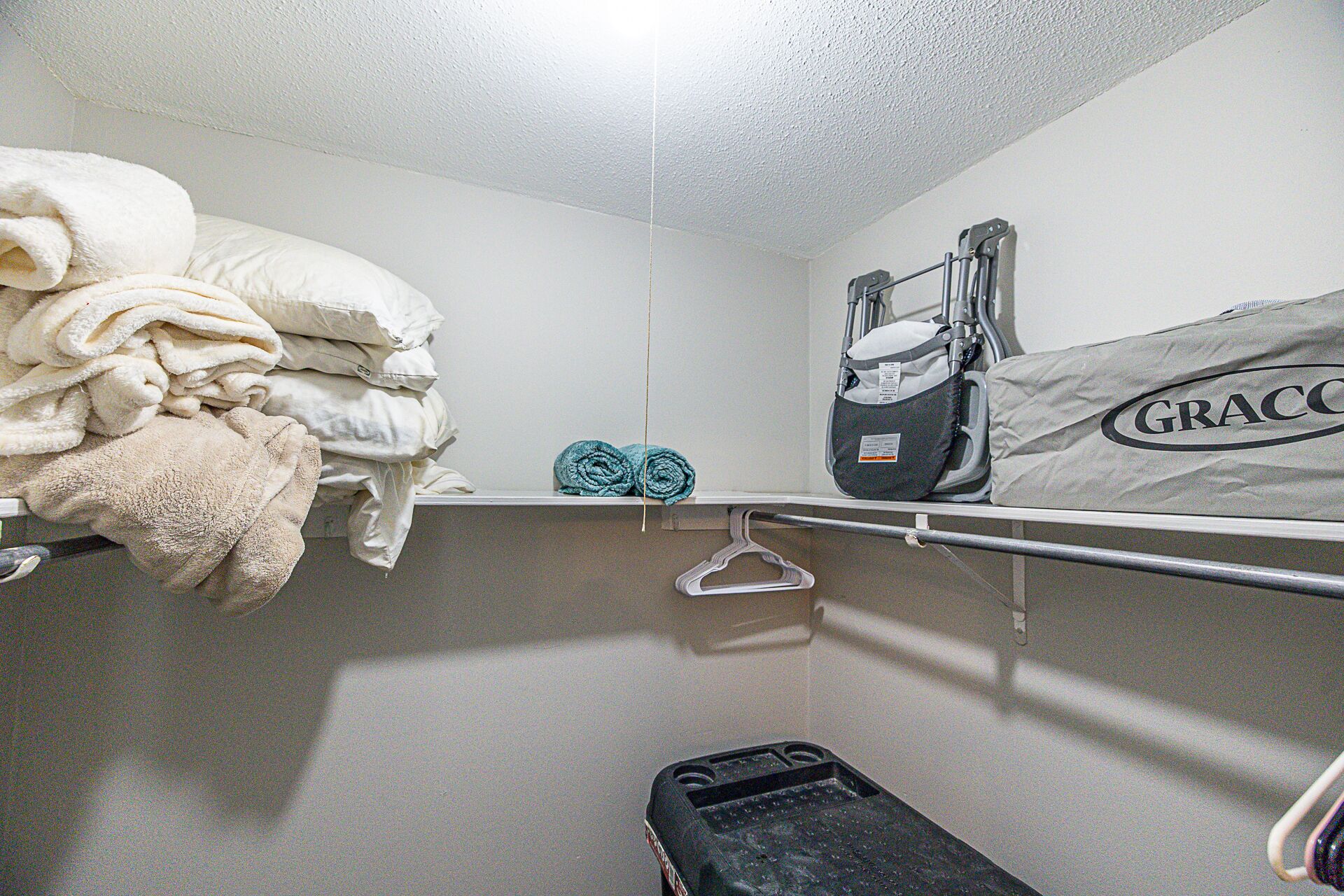 Une petite salle de bain compacte avec un espace de douche blanc, un porte-serviettes avec des serviettes pliées, un siège de douche noir et portable, et un sac étiqueté « GRACCO » accroché au mur.
